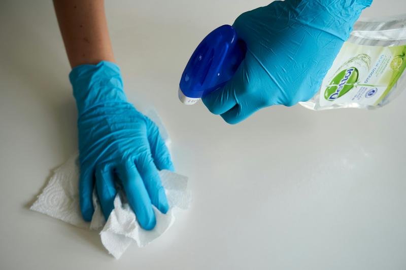 Gloved hands spraying and wiping a white worktop